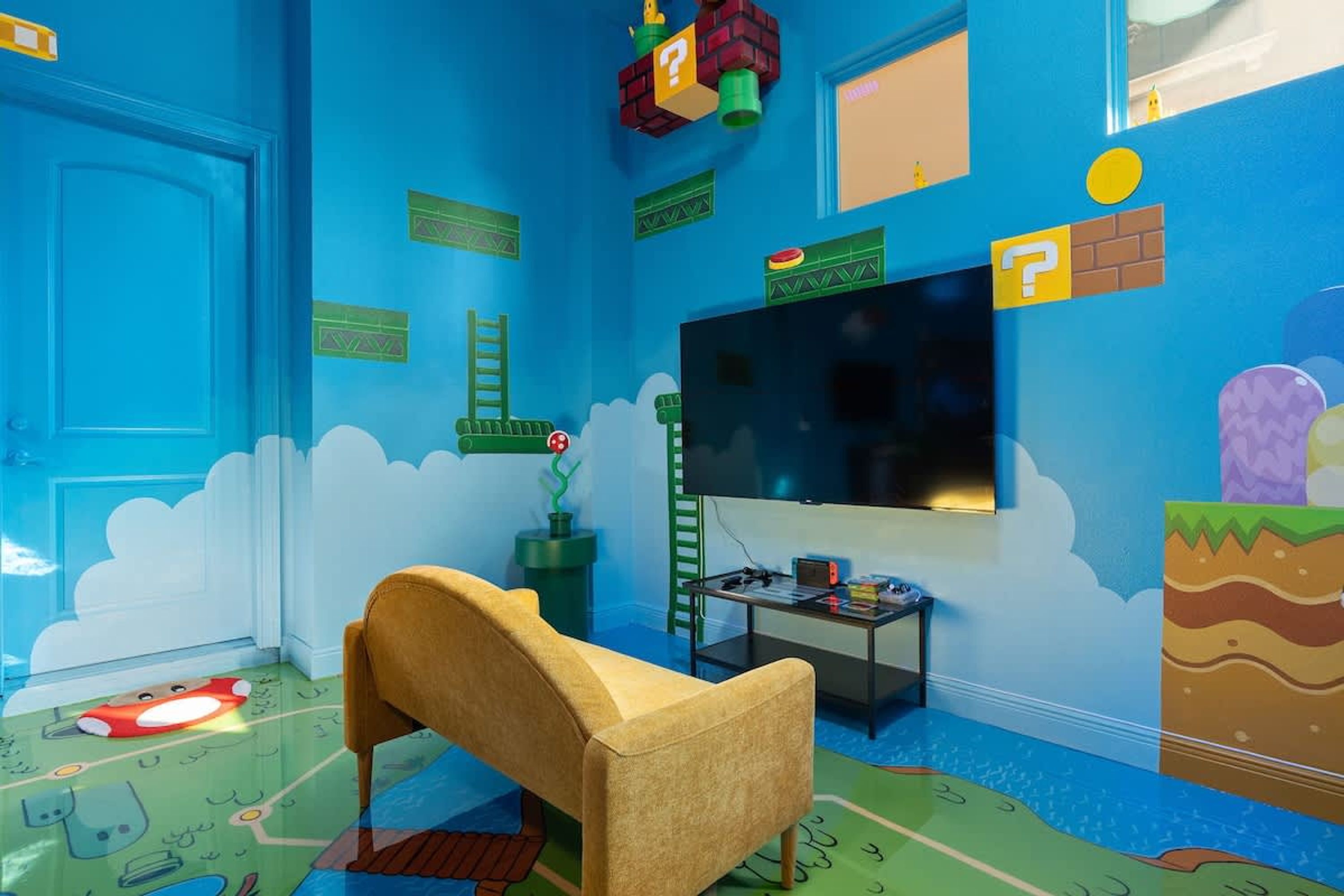 Een kamer met een televisie, een bank, een kleine tafel en een kleurrijke wand met diverse decoraties.