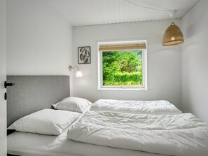Ein Schlafzimmer mit einem Bett, einer Nachttischlampe, einem Fenster mit Blick auf Grünflächen und einer Pendelleuchte.