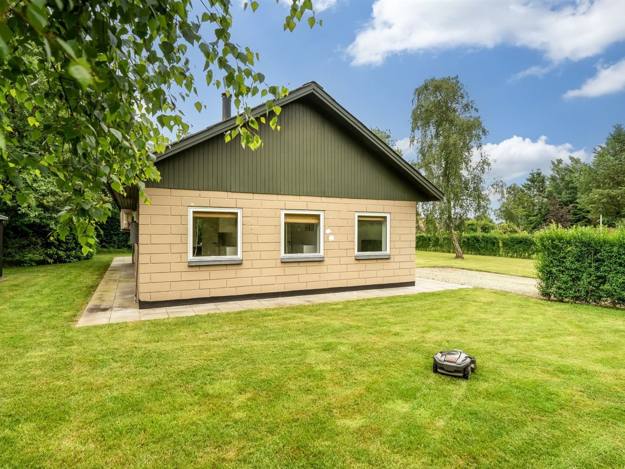 A modern house with a green roof, beige walls, and a well-maintained lawn.