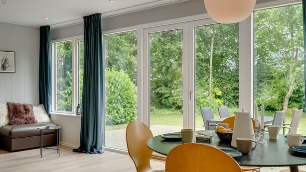 A modern living room with a sofa, a dining table with chairs, and large windows offering a view of the outdoors. - "Adisl" - 300m to the fjord by Interhome (Højslev)