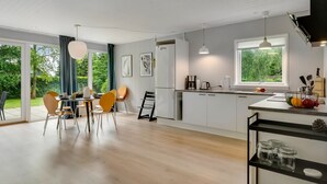 A modern kitchen with white cabinets, a dining area with wooden chairs, and a view of greenery outside. - "Adisl" - 300m to the fjord by Interhome (Højslev)