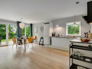 Eine moderne Küche mit weißen Schränken, ein Essbereich mit Holzsesseln und Blick ins Grüne.