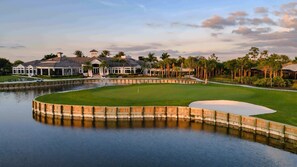 A golf course with a water hazard, a sand bunker, and a clubhouse with a covered driving range. - Completely Remodeled-Fully Furnished Modern 2BR/2BTH-Country Club Membership (Fort Myers)