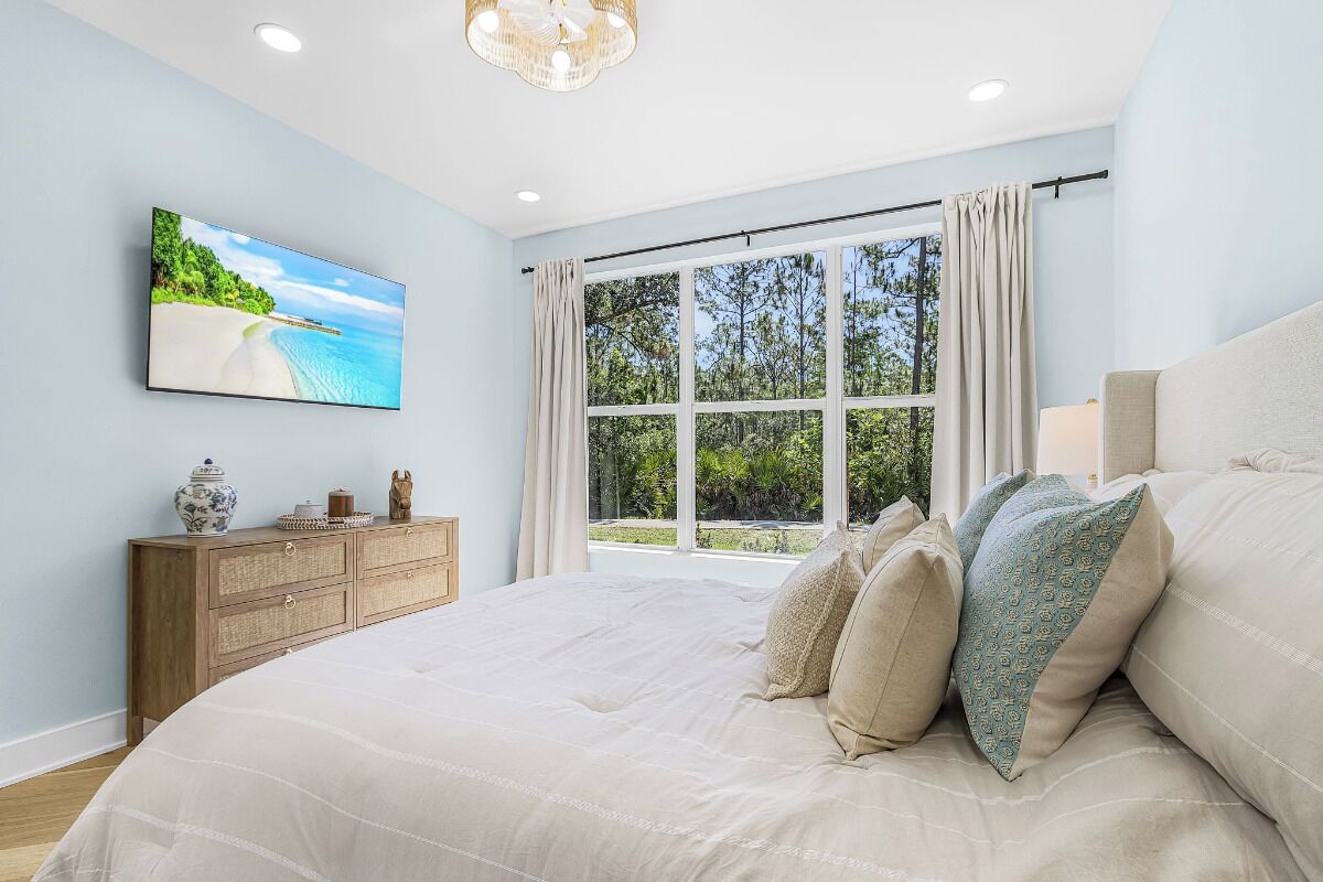 A bedroom with a large bed, a TV on the wall, a wooden dresser, and a window with curtains.