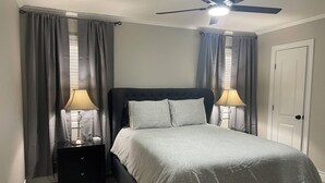 Een slaapkamer met een bed, twee nachtkastjes met lampen, een plafondventilator en een deur.