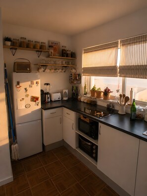 Une cuisine équipée d’un réfrigérateur, d’un four à micro-ondes, d’un four traditionnel et de divers ustensiles de cuisine disposés sur le plan de travail.