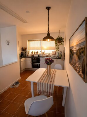 Une cuisine moderne avec un coin repas, comprenant un luminaire suspendu, un tableau au mur et un sol carrelé.