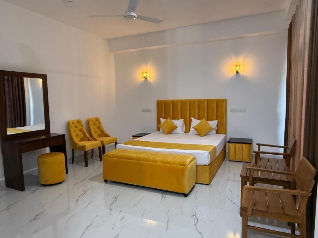 Habitación de hotel con una cama grande, dos sillas, un sillón de madera, una mesita, un espejo y un ventilador de techo.