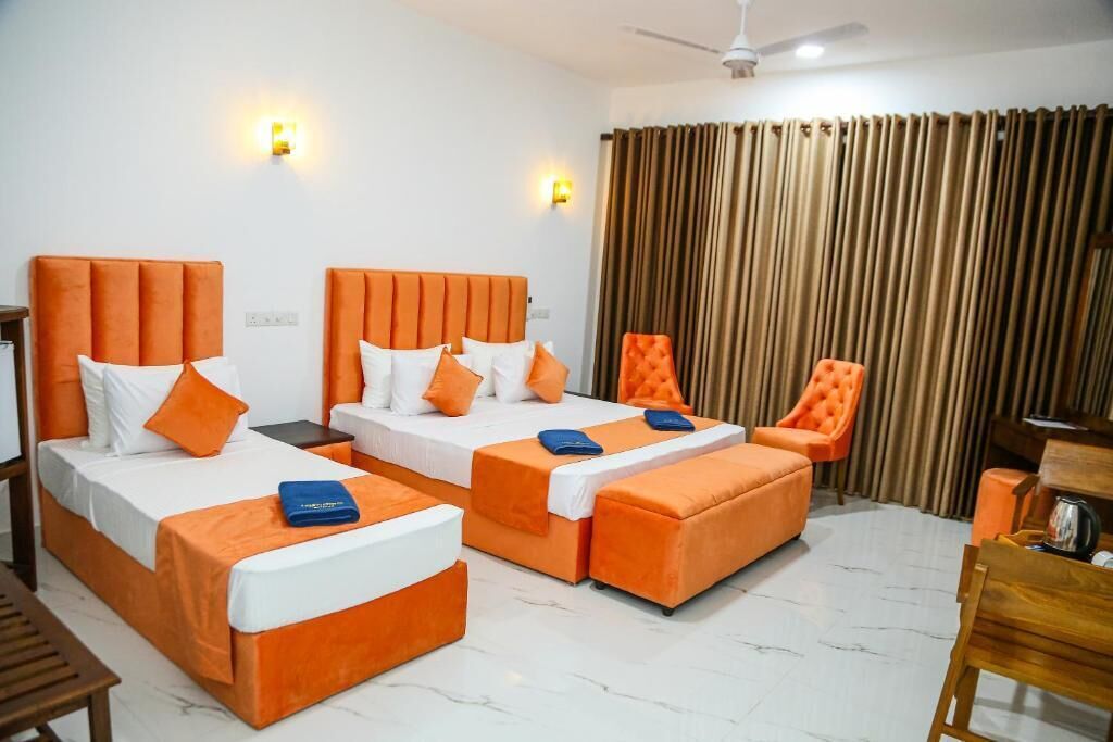 A hotel room with two beds, a chair, a desk, and a curtain.