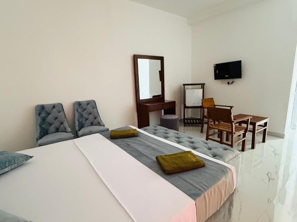 A hotel room with a bed, two armchairs, a desk, a television, and a mirror.