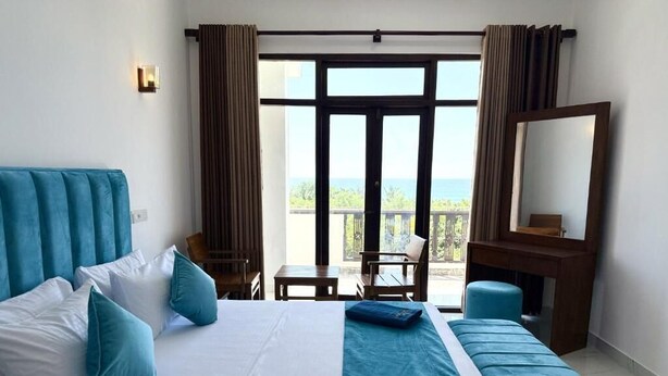 Habitación de hotel con cama, escritorio, silla, vista al balcón y un espejo grande.