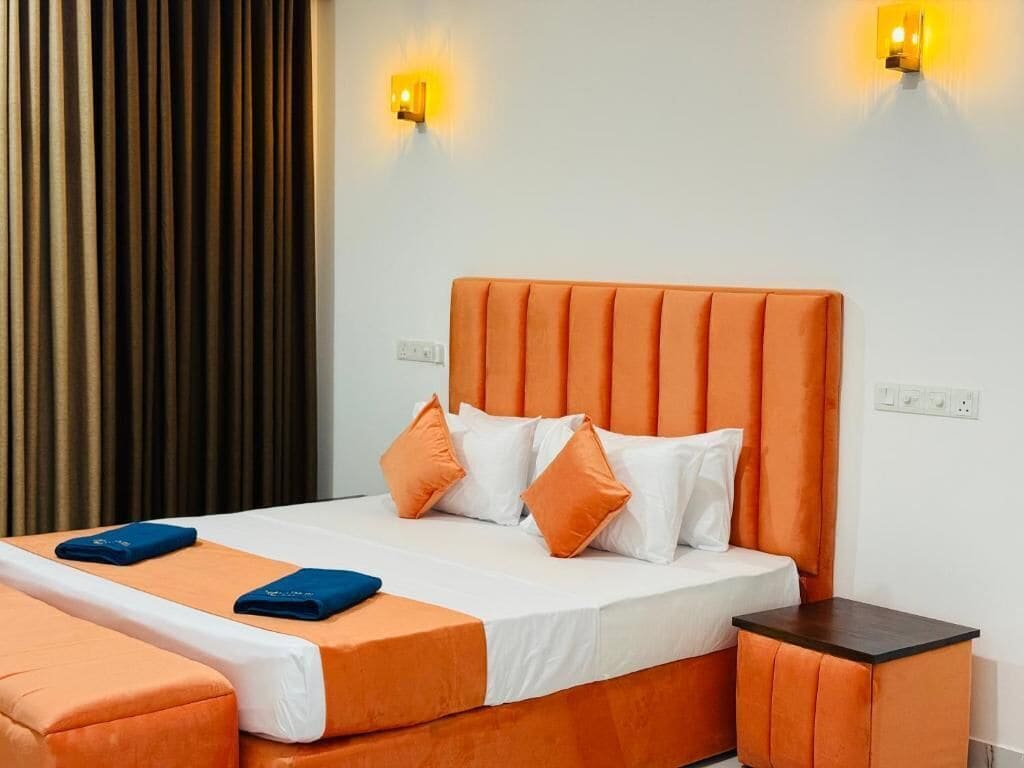 A hotel room with an orange upholstered bed, white bedding, and two wall-mounted light fixtures.