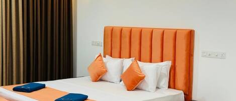 A hotel room with an orange upholstered bed, white bedding, and two wall-mounted light fixtures.