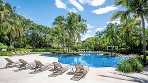 A swimming pool with lounge chairs and palm trees. - Villa Lima – Relaxing 2-Bedroom Oasis in Hacienda Pinilla (Hacienda Pinilla)
