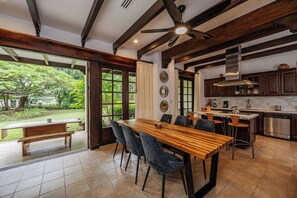 Ein Essbereich mit Holztisch und -stühlen, eine Küche mit modernen Geräten und Blick auf einen Garten.