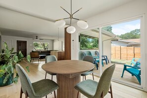 A modern dining area with a round table and chairs, a ceiling fan, and a view of the backyard through large sliding doors. - Travis Height/SoCo - 60s Charm, Modern Soul (Austin)
