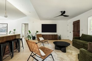 A modern living room with a large flat-screen TV, a ceiling fan, and a bar area with stools. - Travis Height/SoCo - 60s Charm, Modern Soul (Austin)