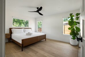Ein Schlafzimmer mit einem Bett, einem Deckenventilator, zwei Fenstern und einer Topfpflanze.