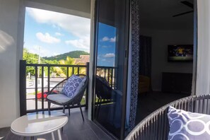 A balcony with a chair and table, a TV in the background, and a view of a street and greenery. - Luxury 9 Bedroom Villa, Ironshore Montego Bay (Montego Bay)