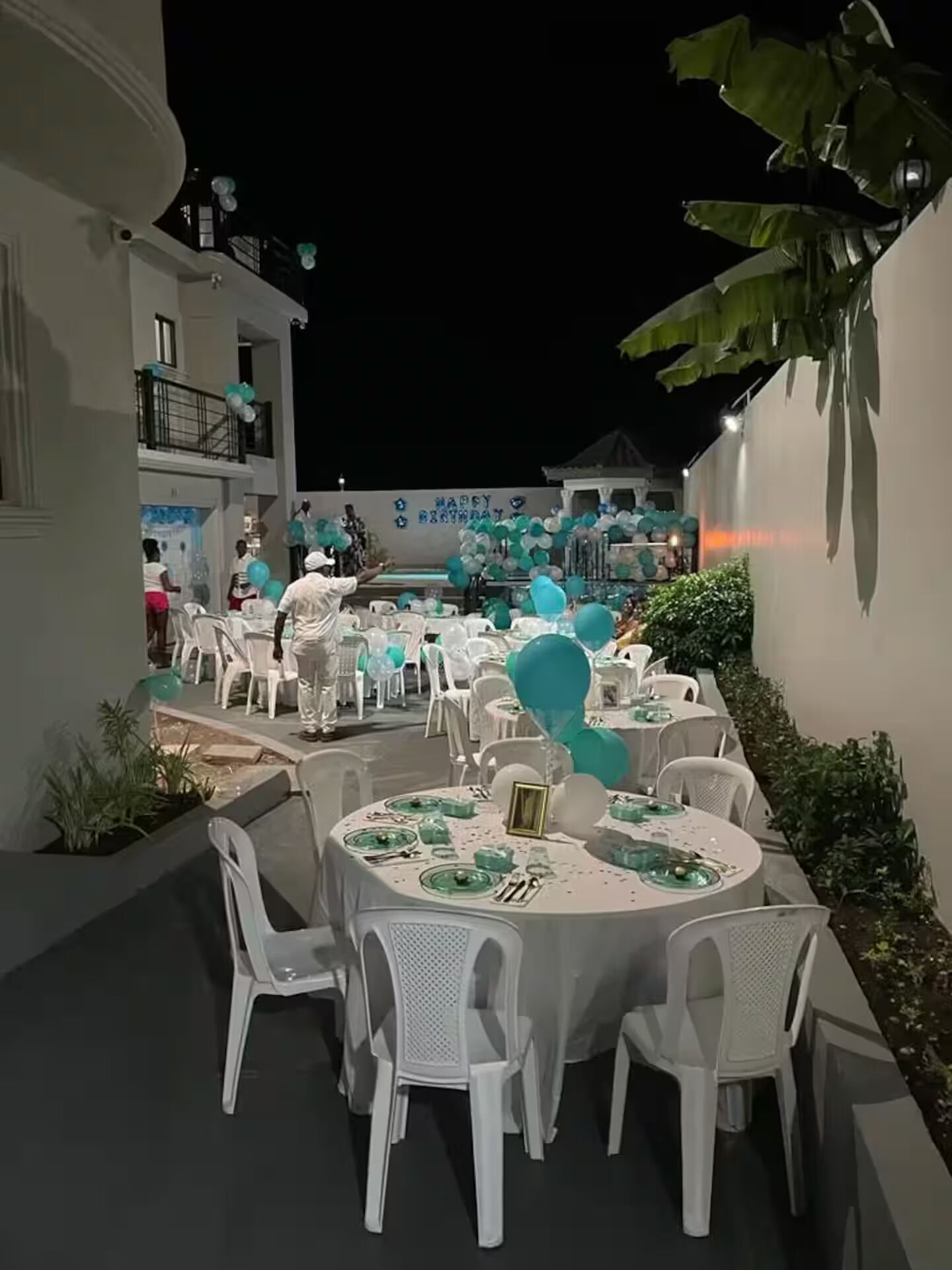 Un área de comedor al aire libre con mesas redondas, sillas blancas y decoración azul aguamarina.