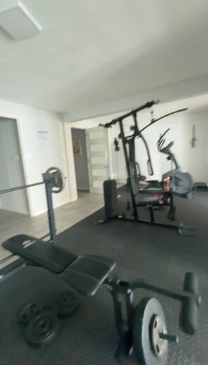 Ein Fitnessstudio mit Langhantelbank, Gewichtsständer und verschiedenen Trainingsgeräten.