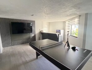 Ein modernes Zimmer mit Tischtennisplatte, Flachbildfernseher und einem Fenster mit Jalousien.
