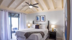 Une chambre à coucher avec un lit, deux tables de chevet avec des lampes, un ventilateur de plafond et des œuvres d’art accrochées au mur.