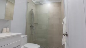 Een moderne badkamer met een douchecabine van glas, een toilet, een wastafel met toiletartikelen en een spiegel boven de wastafel.
