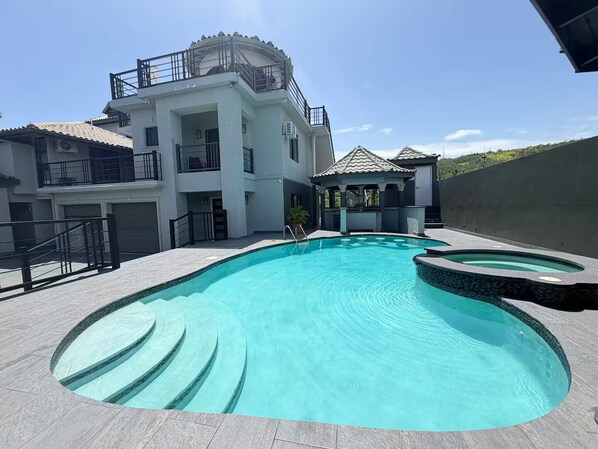 A swimming pool with a curved design, a covered gazebo, and a multi-story building with balconies. - 3 Bedrooms, Ironshore Montego Bay (Montego Bay)