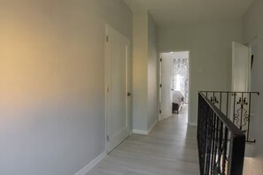 Ein Flur mit einer Treppe, einer Tür zu einem Raum mit floralen Vorhängen und einem Geländer.