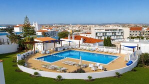 A rooftop pool with lounge chairs, a pergola, and a view of the cityscape.