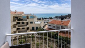 A balcony with a view of a coastal town, buildings with red-tiled roofs, and a clear sky.