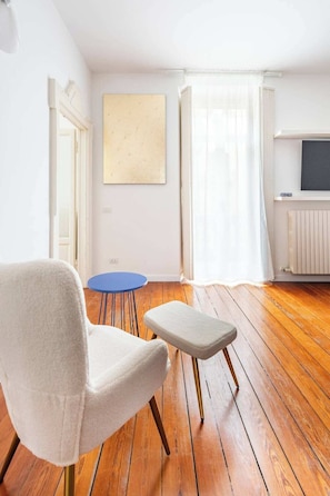 A room with a white armchair, a small round table, and a television on a stand. - Fabulous 2-bedroom apartment with AC in vibrant Milano-Bocconi area (Milano)