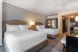 Habitación de hotel con dos camas, un papel tapiz estampado, un escritorio y un espejo.