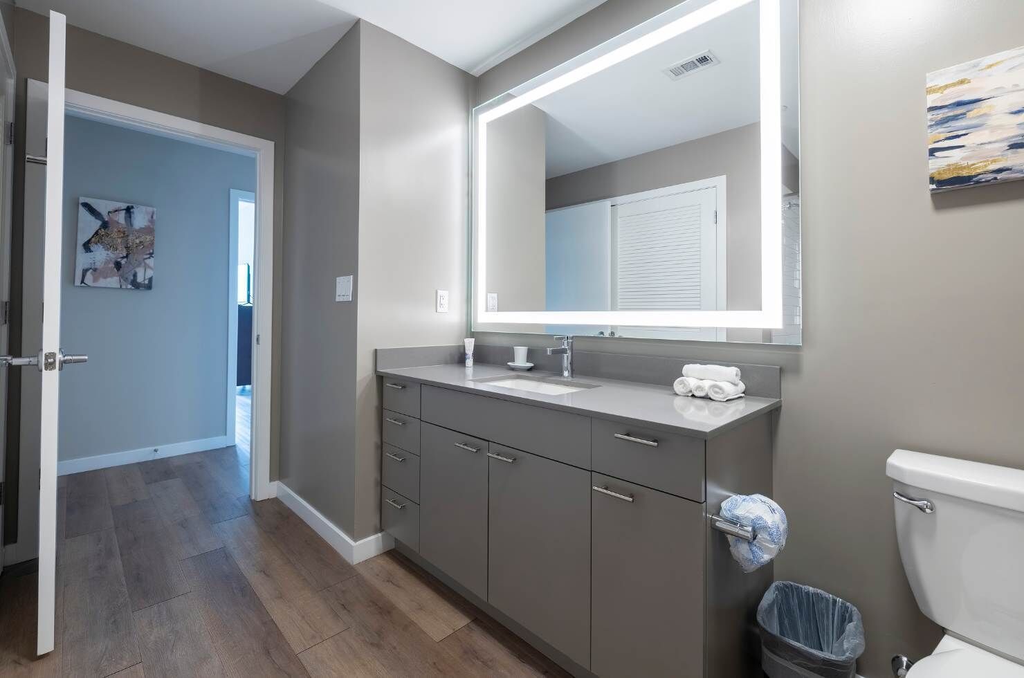 A modern bathroom with a grey vanity, a large mirror, and a toilet.