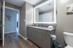 A modern bathroom with a grey vanity, a large mirror, and a toilet. - Waterfront Luxury Living in Harbor Point (Stamford, CT)