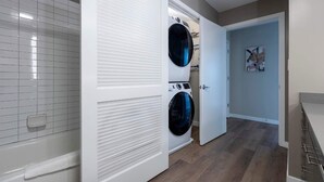 Une buanderie équipée de deux machines à laver et de deux sèche-linge à chargement frontal, d’un mur carrelé et d’une porte donnant sur une autre pièce.
