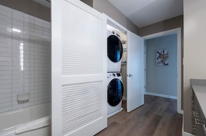 A laundry room with two front-loading washers and dryers, a tiled wall, and a door leading to another room. - Waterfront Luxury Living in Harbor Point (Stamford, CT)