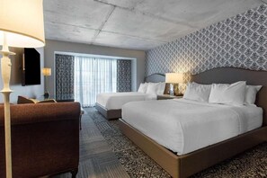 Habitación de hotel con dos camas, un sofá, un televisor y un papel tapiz estampado.