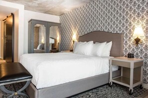 Habitación de hotel con cama, mesitas de noche, un banco, armario y papel tapiz estampado.