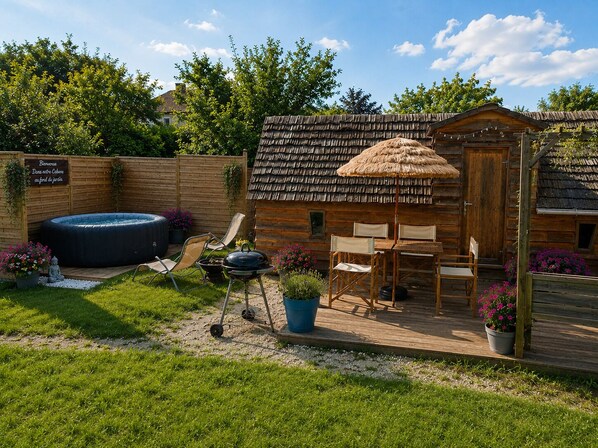 A wooden cabin with a thatched roof, a hot tub, and outdoor seating. - Vrbo Property (Rahon)