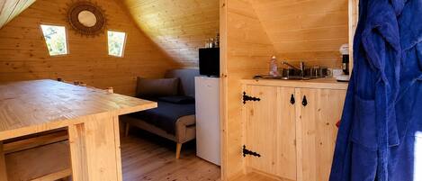 A wooden cabin with a dining table, a sofa, a kitchenette, and a blue robe hanging on the wall.