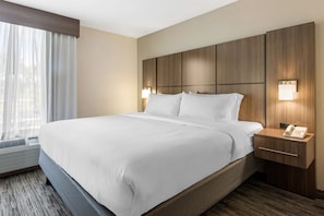 Ein Hotelzimmer mit einem großen Bett, Nachttischlampen, einem Telefon und einem Fenster mit Vorhängen.
