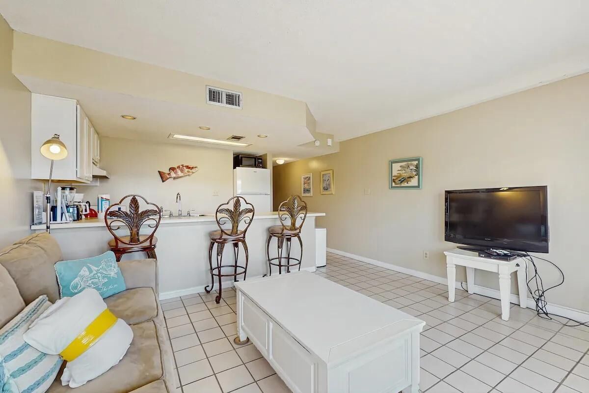Una sala de estar con sofá, mesa de centro, televisor y una zona de cocina con refrigerador y microondas.