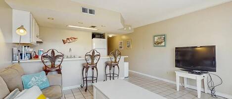 Una sala de estar con sofá, mesa de centro, televisor y una zona de cocina con refrigerador y microondas.
