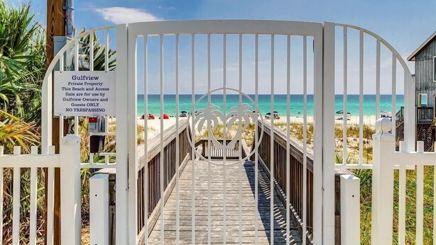 Une entrée fermée par un portail donne accès à une zone de plage, et une passerelle en bois mène à la plage.