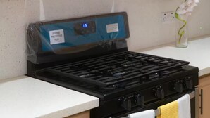 Une cuisine avec des armoires en bois, un four à micro-ondes en acier inoxydable, une cuisinière à gaz et un petit vase avec des fleurs posé sur le comptoir.