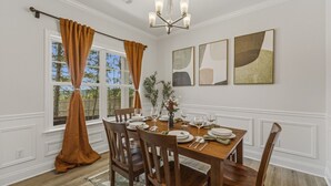 A dining room with a wooden table set for four, white paneled walls, and a chandelier. - Brand new home - The Homestead (Columbus)