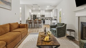 A modern living room with a sofa, a coffee table with candles, a fireplace, and a kitchen in the background. - Brand new home - The Homestead (Columbus)