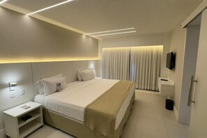 Ein modernes Hotelzimmer mit einem großen Bett, Nachttischen, einem Fernseher und einem fensterbäckischem Fenster.